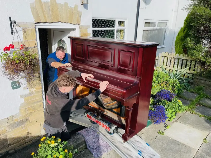 Specialist team moving a mahogany upright piano through a doorway using piano skate equipment